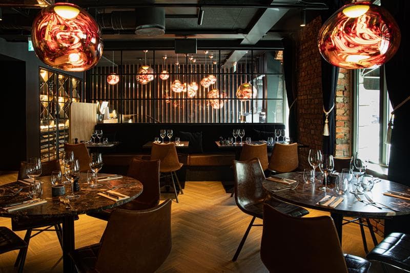 Restaurant interior with round, brown tables, brown chairs and seating section against the wall.