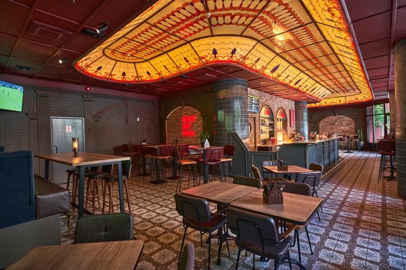 Restaurant interior with small square tables and chairs, bar and decorated glass ceiling above the bar